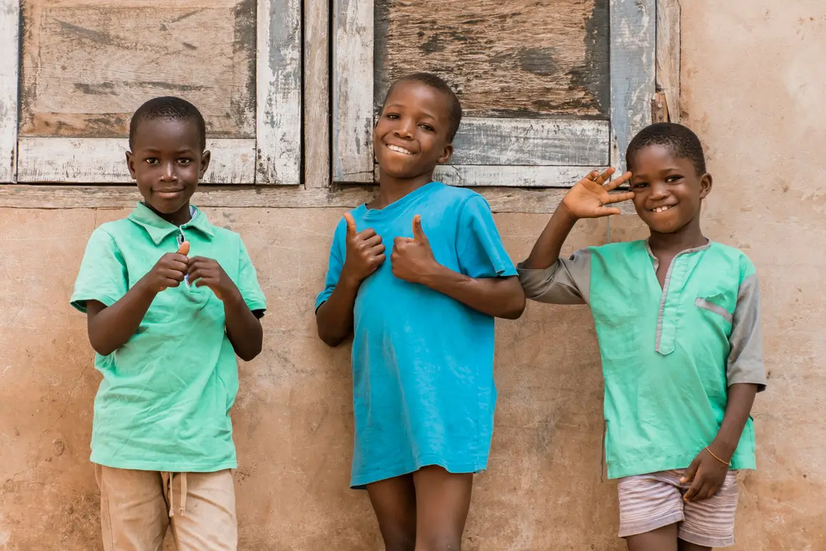 Three boys wearing green shirts stand together in front of a building, smiling and posing for the camera.